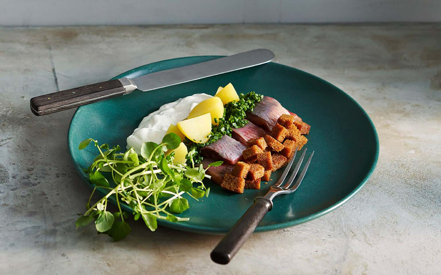 Grönblå lunchtallrik med sill och flera tillbehör.