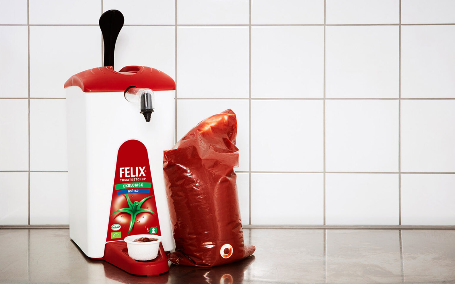 Felix Ekologisk Ketchup Osötad i påse bredvid en Sentomat/dispenser.