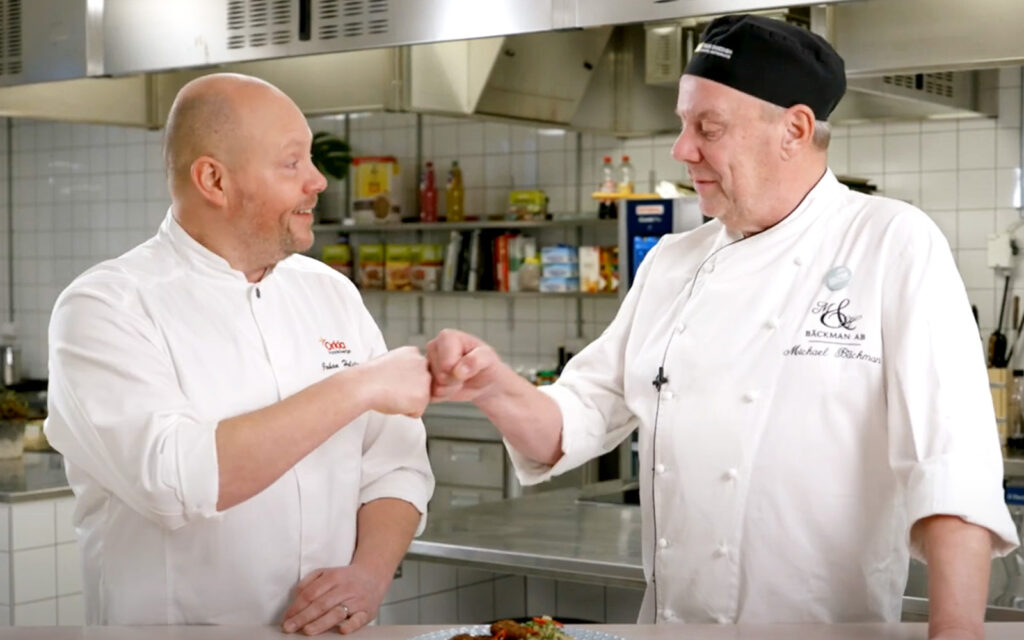Johan Holster och Michael Bäckman diskuterar i köket. De har sina kockkläder på sig.