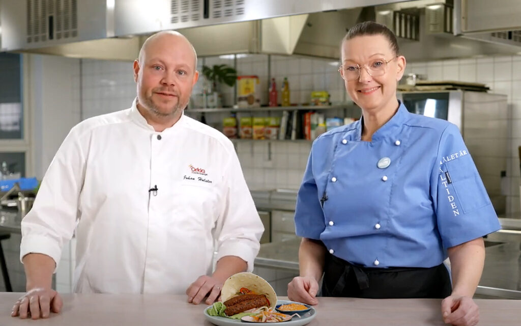 Johan Holster och Sandra Ostwald diskuterar i köket. De har sina kockkläder på sig.