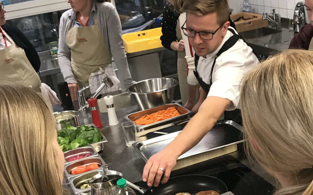 Kocken Marcus undervisar andra människor i ett kök. Han sträcker sig efter en skål med ingredienser.