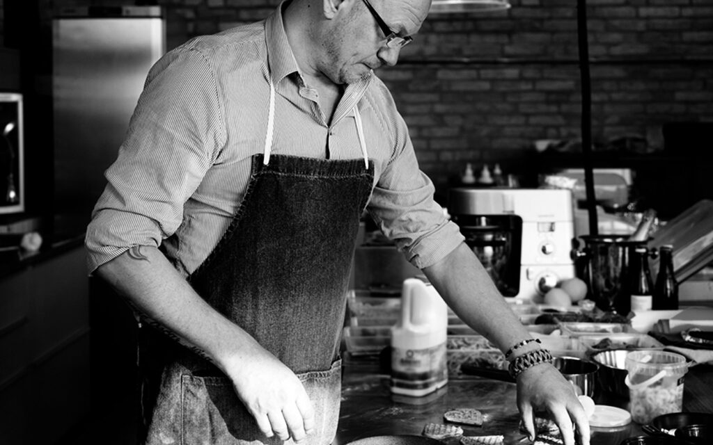 Kocken och kulinariska kreatören Johan Liljegren arbetar vid en bänk i ett kök. Bilden är svartvit.