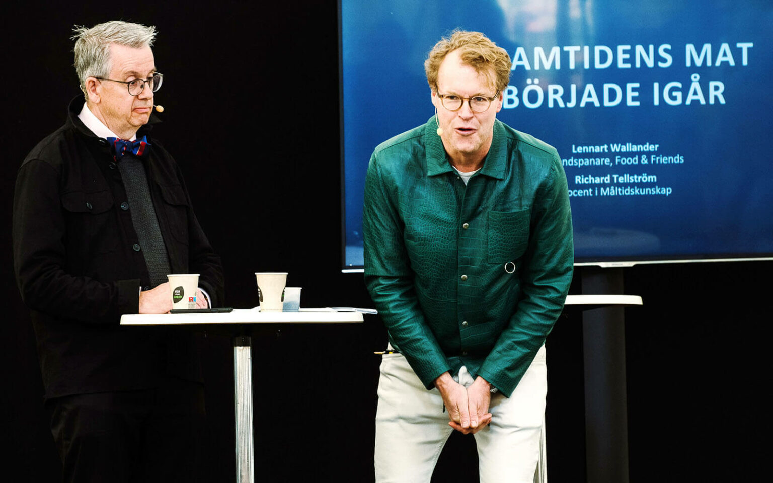 Richard och Lennart på scenen. Lennart står framåtlutad och pratar med publiken.