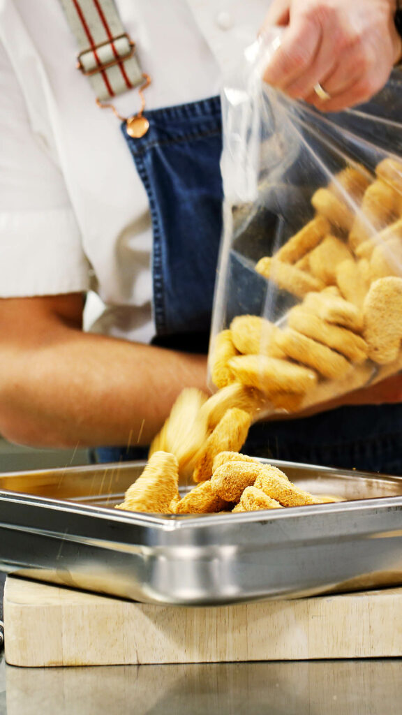 Kock som häller upp nuggets ur en påse ner i ett bleck.