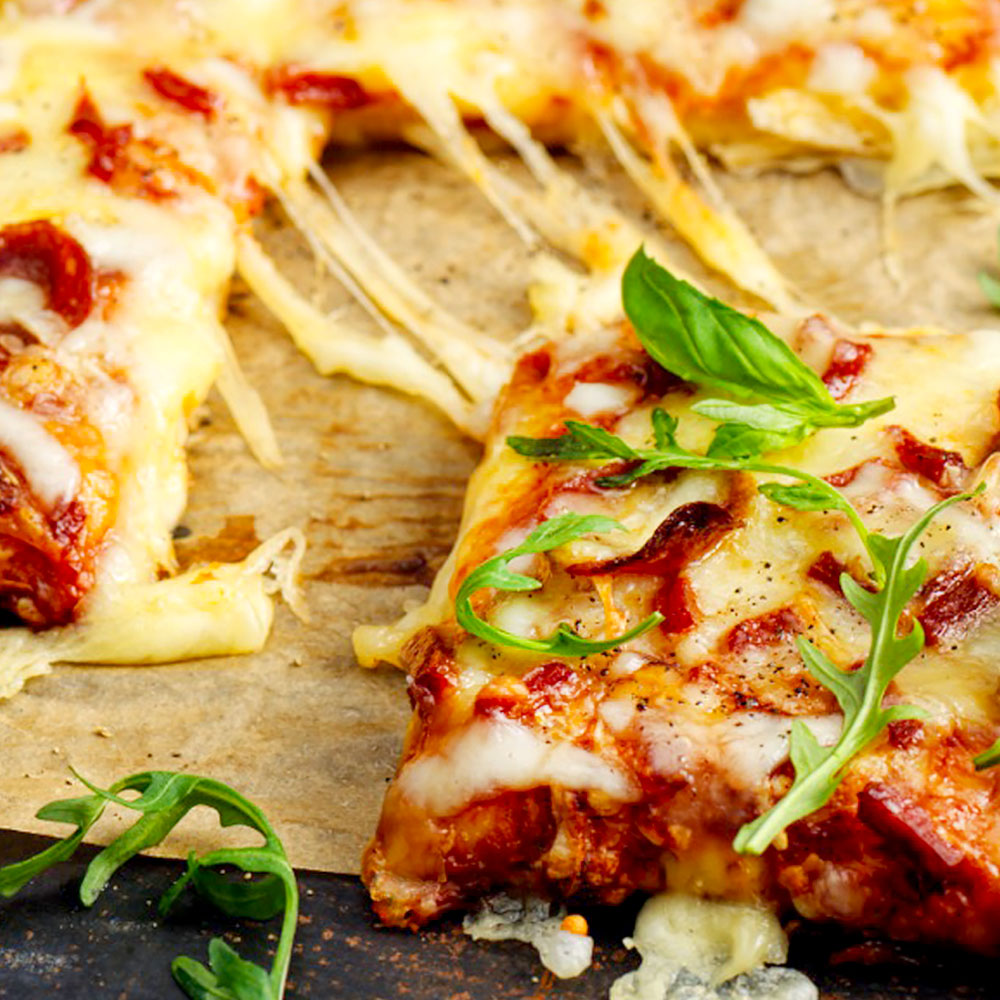 Närbild på pizzabit med strängar av smält ost kopplade till övriga pizzan.
