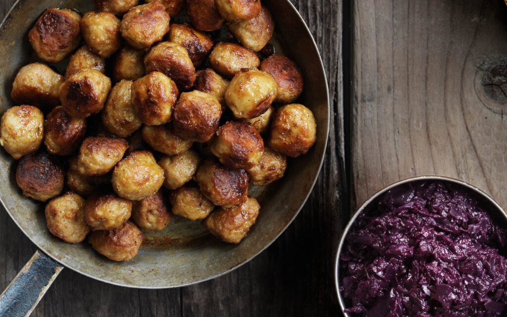 Köttbullar i stekpanna och rödkål i en skål.