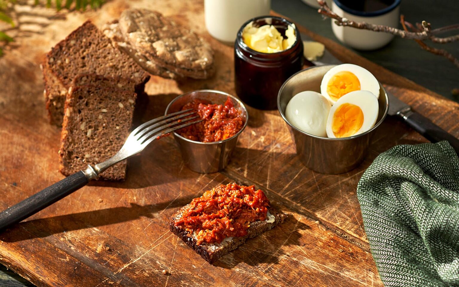 Abba grovhackad makrillfilé i tomatsås på en träbricka. Dels på en smörgås, men också i en liten skål. Ägg, bröd och smör syns bredvid.