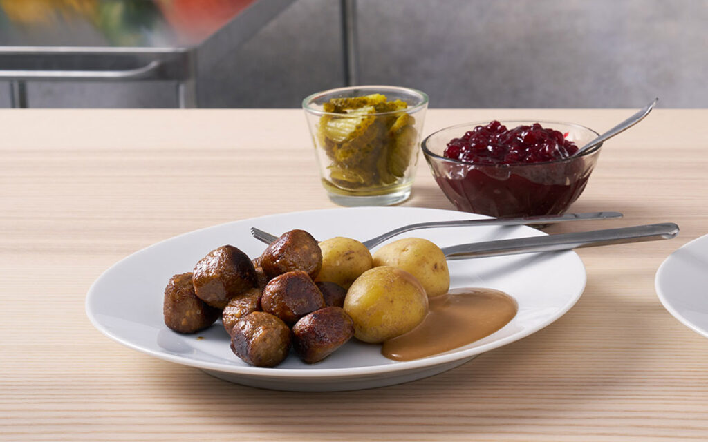 FELIX Nötköttbulle med ärta på en tallrik med brunsås och potatis. Lingonsylt och inlagd gurka i skålar i bakgrunden.