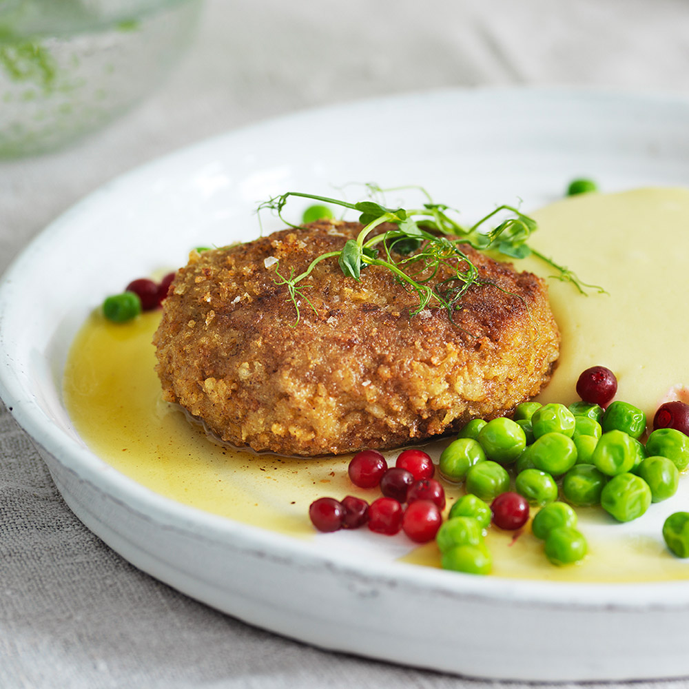 Närbild på biff gjord med Anamma Baljväxtfärs, serverad med sås, lingonsylt och gröna ärtor.