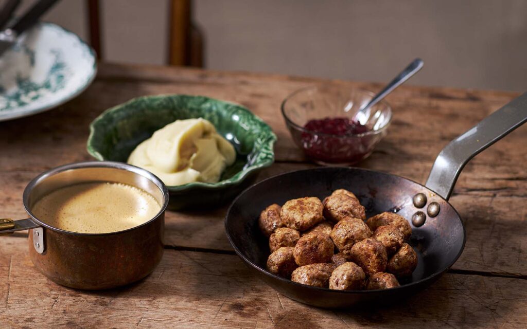 50/50-bullar, brunsås, potatismos och lingonsylt i olika skålar/kastruller/stekpannor på ett träbord.