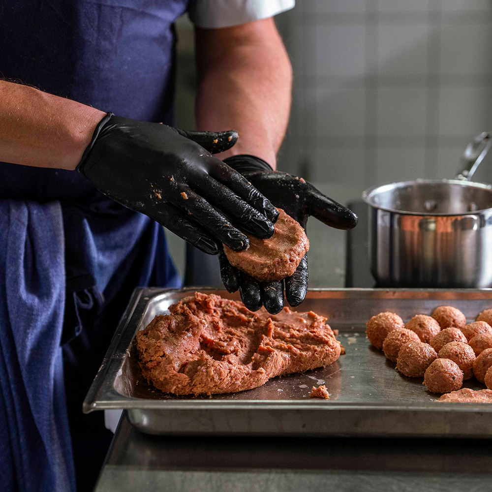 Närbild av kockhänder som rullar köttbullar av 50/50-färs och lägger på en plåt.