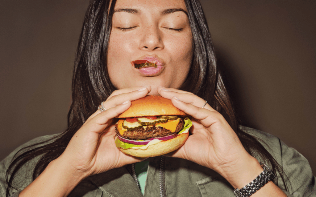 Tjej som äter burgare med FELIX Dillpicklad Gurka och andra tillbehör.