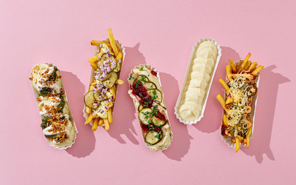 Avlånga engångstallrikar med fem olika serveringar av pommes och mos. Serverade mot rosa bakgrund.