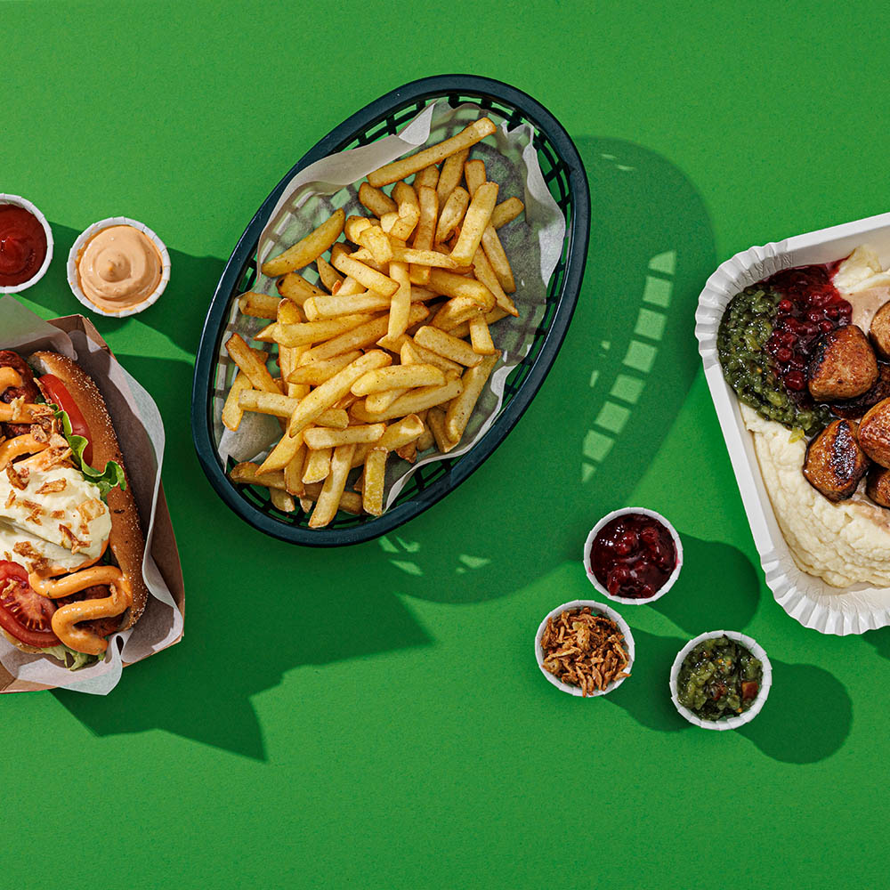 Korv, pommes, såser, tillbehör, mostallrik med köttbullar serverade mot grön bakgrund.