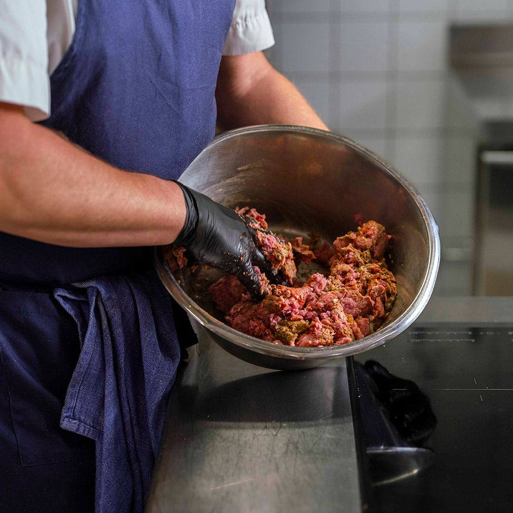 Närbild på kock som mixar växtbaserad färs med animalisk färs i en rostfri bunke.