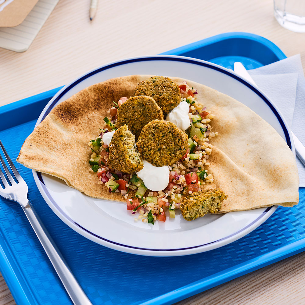 Lecora Falafel serverad på bröd, på en blå bricka i skolmiljö.